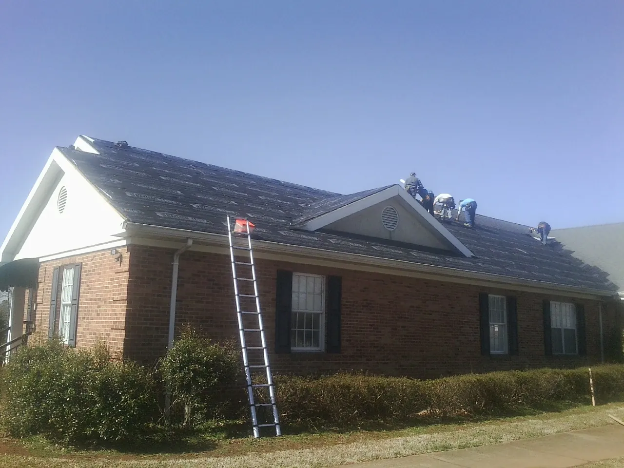 Crew tearing shingles off a brick ranch roof with a ladder set — Emergency Roof Repair work by our crew in Deep Gap