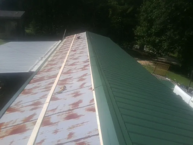 Old rusted panels beside newly installed green metal roofing — Wind Damage Roof Repair by Roofing Brothers in Deep Gap