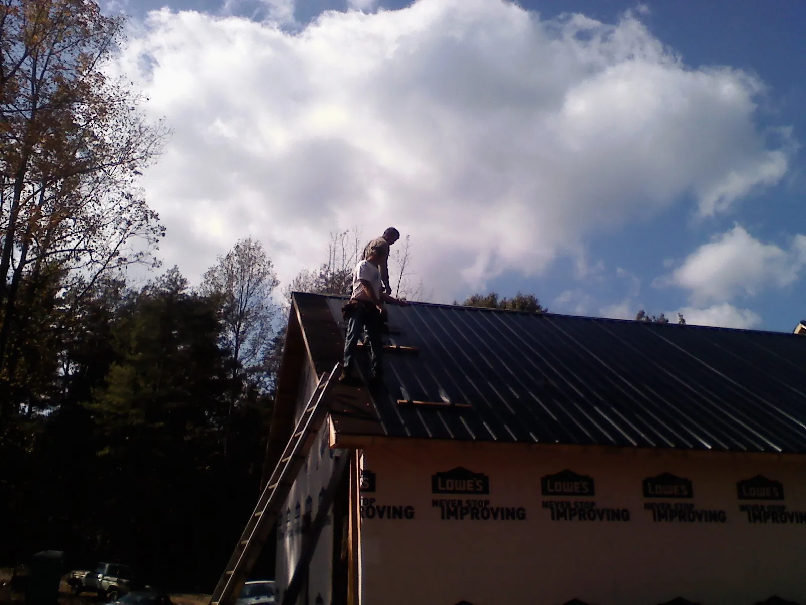 Roofer fastening dark metal panels high against a cloudy sky, from a Roof Inspection job in Deep Gap