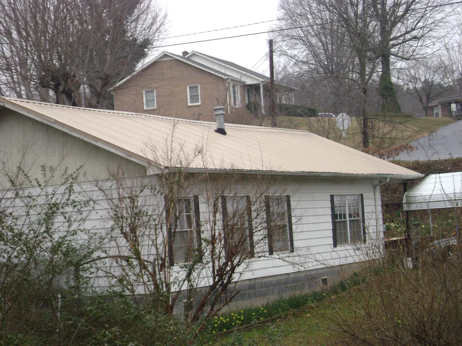 Tan metal roof on a white sided house set into a hillside — Commercial Roofing by Roofing Brothers in Deep Gap